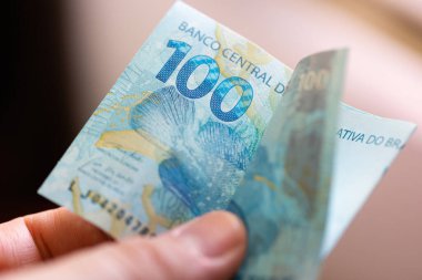 Bir adamın eli 100 Brezilyalı Real banknotunu tutuyor. Yakın çekim..