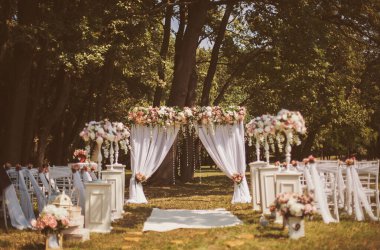 Dışarıda çiçekli düğün dekoru. Düğün töreni. Düğün alanında, ormanda duran pembe ve beyaz çiçeklerle süslenmiş kemer. Güzel bir düğünde konuklar için koltuklar..