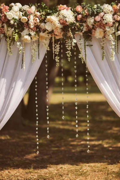 decor of a wedding arch, white sparkling threads for a wedding arch. Wedding decor outside with flowers. Wedding ceremony. Arch, decorated with pink and white flowers standing in the woods.