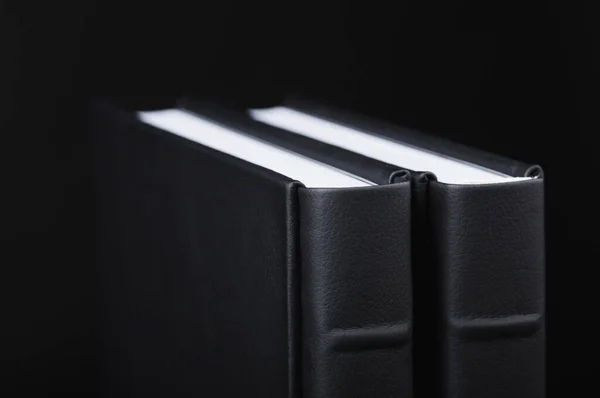 A beautiful leather bound books against a black background. Two books with black blank cover. Stylish books on dark black background. The texture of the cover of a photobook made of genuine leather.