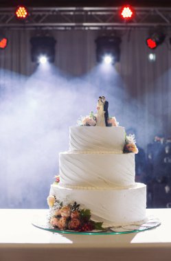 Düğün pastası. Düğün partisinde süslemeli düğün pastası. Beyaz, üç katlı, çiçeklerle süslenmiş..