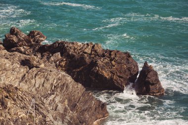 Mavi denizde taşlar, kayalık plajlar, yazın günbatımında dalgalar Liguria, İtalya 'da. Tropikal arka plan. Şeffaf gök mavisi su ve taşlar.