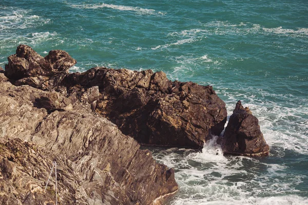 Mavi denizde taşlar, kayalık plajlar, yazın günbatımında dalgalar Liguria, İtalya 'da. Tropikal arka plan. Şeffaf gök mavisi su ve taşlar.