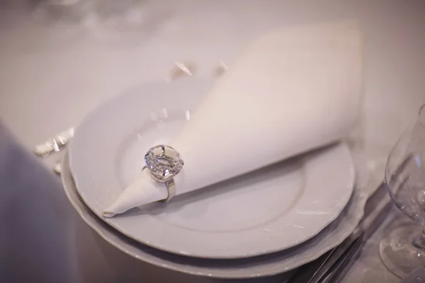 Plate for elegant wedding dinner. White napkin on white table. Beautiful table setting. A beautifully set table for a festive dinner. Wedding banquet. Plate, napkin with a ring.