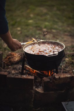 Kamp ateşinin üstünde turist var. Saha koşullarında yemek pişirmek, piknikte kamp ateşinde demlik pişirmek. Açık havada yemek pişirmek için bir kazan yanıyor. Ateşte çorba. Yemek dışarıda. Çaydanlık kebabı..