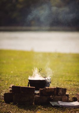 Kamp ateşinin üstünde turist var. Saha koşullarında yemek pişirmek, piknikte kamp ateşinde demlik pişirmek. Açık havada yemek pişirmek için bir kazan yanıyor. Ateşte çorba. Yemek dışarıda. Çaydanlık kebabı..