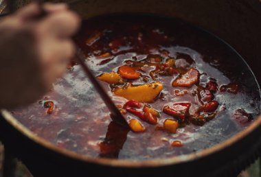 Kamp ateşinin üstünde turist var. Saha koşullarında yemek pişirmek, piknikte kamp ateşinde demlik pişirmek. Açık havada yemek pişirmek için bir kazan yanıyor. Ateşte çorba. Yemek dışarıda. Çaydanlık kebabı..