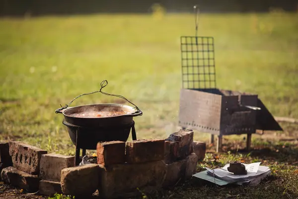 stock image Tourist pot over camp fire. Cooking in field conditions, boiling pot at the campfire on picnic. A cauldron for cooking is on the fire in the open air. Soup on a fire. Food outdoors. Kettle goulash.