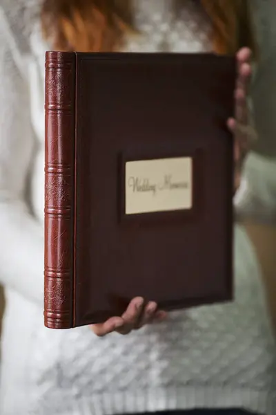 Female hands holding square photo book for wedding album. Wedding photo book, family album. Photo books with embossing and a cover of genuine leather. A book in an expensive binding.