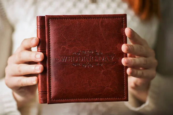 Female hands holding square photo book for wedding album. Wedding photo book, family album. Photo books with embossing and a cover of genuine leather. A book in an expensive binding.