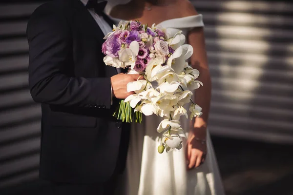 Wedding couple holding bouquet. Elegance wedding decorations. Wedding bouquet for the bride and groom at an event. the bride and groom are standing close to each other in sun light with bouquet.