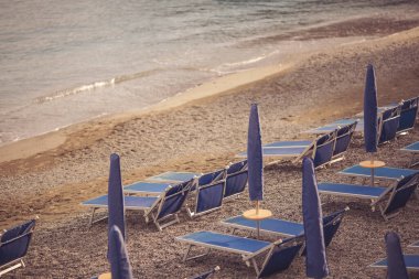 Sezon öncesi İtalya 'nın Adriyatik kıyısında güneşli yataklı ve şemsiyeli terk edilmiş bir sahil. Plaj sezonu kapanıyor. Seçici odaklanma. İnsansız kumsal. Kaybolan güneşlik şemsiyeleri.