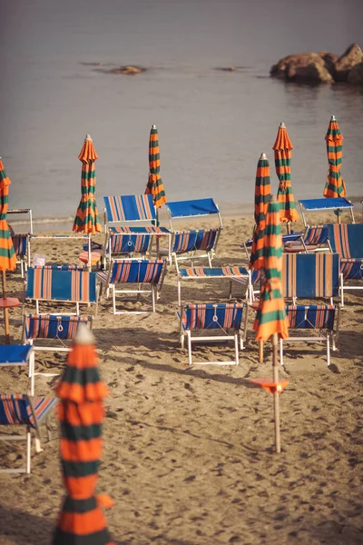 Deserted beach with sunbeds and umbrellas at the Italian Adriatic coast in the preseason, Italy. Closing beach season concept. Selective focus. sandy beach without people. losed sunshade parasols.