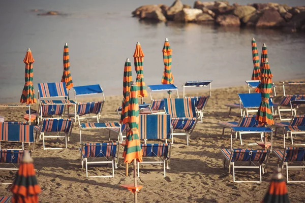 Deserted beach with sunbeds and umbrellas at the Italian Adriatic coast in the preseason, Italy. Closing beach season concept. Selective focus. sandy beach without people. losed sunshade parasols.