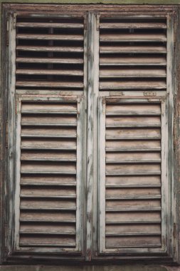 Panjurlu eski ahşap pencere, çatlamış betonlu kır evi. Kapalı ahşap pencere çerçevesi, eski çatlak boya. Kapalı panjurlu klasik pencere. Ahşap pencere kepengi ve soyulmuş boya..