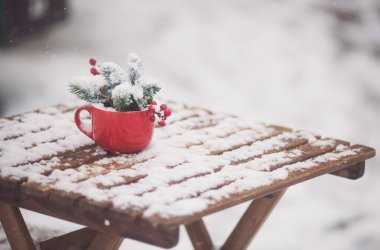 Kırmızı fincanda ladin dalları ve karlı ahşap masa üzerinde kırmızı böğürtlen var. Masası, sandalyeleri ve Noel süslemeleri olan bir Noel terası. Karlı bir kış sokak sahnesi. Noel havası.