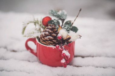 Kırmızı fincanda ladin dalları ve karlı ahşap masa üzerinde kırmızı böğürtlen var. Masası, sandalyeleri ve Noel süslemeleri olan bir Noel terası. Karlı bir kış sokak sahnesi. Noel havası.