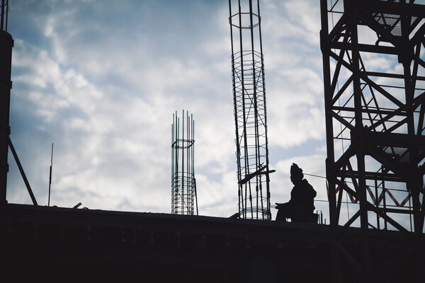 Silhouette of worker on building site, construction site at sky in evening time. Construction welder working high at a structure in the evening. Silhouette welder on steel roof structure.