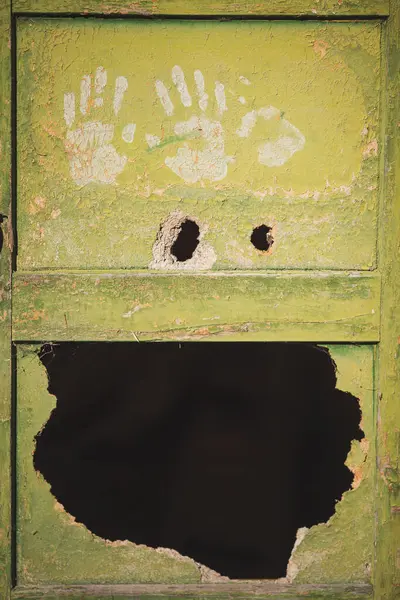 Big hole and painted imprint of hands on a green wooden door. Old broken door with a big gap and human palm marks. Horror and terror concept. Nightmares of scary fear, danger.
