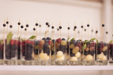 Bardakta meyve ve böğürtlen. Ziyafette yemek servisi. Bardakta böğürtlen ve çilek. Düğünde yemek servisi. Düğün ziyafeti masası. Meyveli tatlı masa, düğün yemekleri. Partide meyveli çikolata.