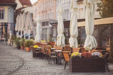 Şemsiyeler ve barın masaları. Kafe kafe restoranının terasında. Tahta sandalyeler ve masalar. Açık teras. Antika sandalyeleri ve masaları olan eski moda boş kafe terası. Çatı katı tarzı kafe.