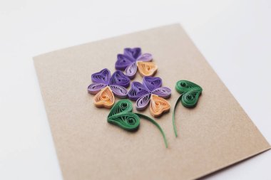 Kahverengi kağıtta menekşe çiçekli tüy kalem kartı. Bahar çiçekleri. Kağıt kalem tekniğindeki tebrik kartlarından yapılmış bir el. Evde el işi. Hobi, ev ofisi..