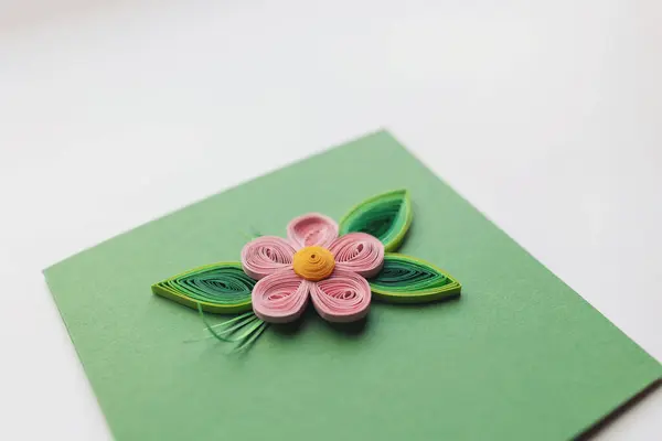 quilling card with pink apple flower on green paper background. Spring flowers. Hand made of greeting cards in paper quilling technique. Handicraft at home. Hobby, home office. Selective focus.
