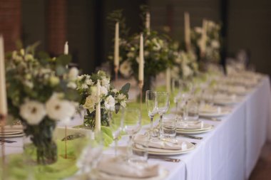 Şenlikli yemek için şık bir masa. Sandalyeler ve masa misafirler için, çatal bıçak takımı, yeşillik çiçekleri ve çanak çömlek ile servis ediliyor ve beyaz bir masa örtüsüyle kaplanıyor. Düğünde yemek servisi. Ziyafet..