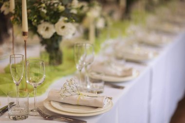 Şenlikli yemek için şık bir masa. Sandalyeler ve masa misafirler için, çatal bıçak takımı, yeşillik çiçekleri ve çanak çömlek ile servis ediliyor ve beyaz bir masa örtüsüyle kaplanıyor. Düğünde yemek servisi. Ziyafet..
