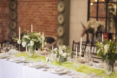 Şenlikli yemek için şık bir masa. Sandalyeler ve masa misafirler için, çatal bıçak takımı, yeşillik çiçekleri ve çanak çömlek ile servis ediliyor ve beyaz bir masa örtüsüyle kaplanıyor. Düğünde yemek servisi. Ziyafet..