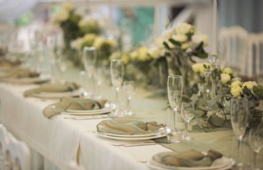 Şenlikli yemek için şık bir masa. Sandalyeler ve masa misafirler için, çatal bıçak takımı, yeşillik çiçekleri ve çanak çömlek ile servis ediliyor ve beyaz bir masa örtüsüyle kaplanıyor. Düğünde yemek servisi. Ziyafet..