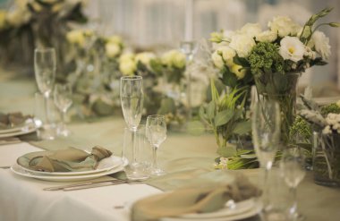 Şenlikli yemek için şık bir masa. Sandalyeler ve masa misafirler için, çatal bıçak takımı, yeşillik çiçekleri ve çanak çömlek ile servis ediliyor ve beyaz bir masa örtüsüyle kaplanıyor. Düğünde yemek servisi. Ziyafet..