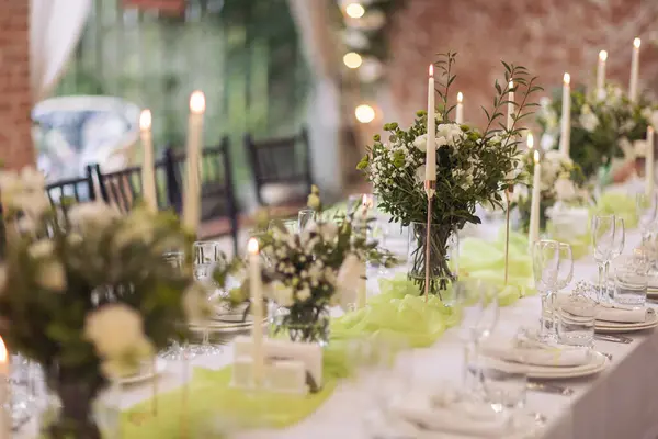 Stylish elegant table setting for festive dinner. The chairs and table for guests, served with cutlery, greenery flowers and crockery and covered with a white tablecloth. Catering on Wedding. Banquet.