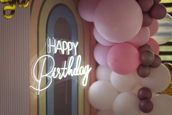 Happy birthday neon lettering sign shining between balloons. Photo zone decoration from balloons on a baby party in a restaurant. lots of gray pink balloons on holiday. birthday holiday celebration