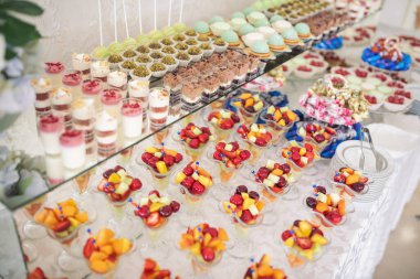 Kokteyl partisi için tabakta servis edilen pek çok küçük kek, tatlı ve meyve. Doğum günü veya düğün yemeği için çikolata. Yemek servisi. Lezzetli bir tatlı. Düğün ziyafeti masası. Partide meyveli çikolata