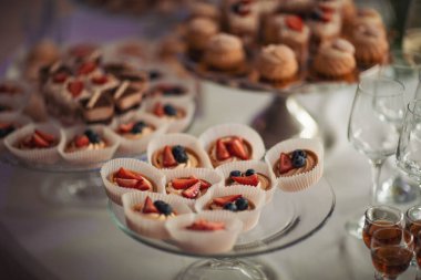Kokteyl partisi için tabakta servis edilen pek çok küçük kek, tatlı ve meyve. Doğum günü veya düğün yemeği için çikolata. Yemek servisi. Lezzetli bir tatlı. Düğün ziyafeti masası. Partide meyveli çikolata