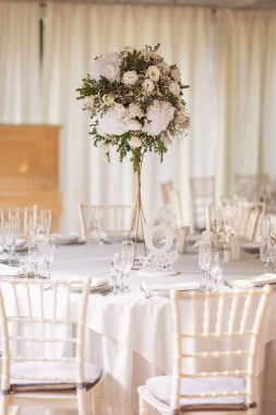 Düğün günü masada güzel çiçekler olacak. Düğün için dekoratif ve zarif çiçeklerle süslenmiş beyaz renkli düğün masası. Düğün masasında çiçekler ve servis tabakları var..