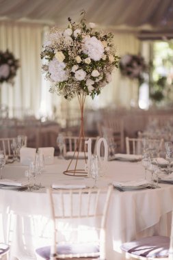 Düğün günü masada güzel çiçekler olacak. Düğün için dekoratif ve zarif çiçeklerle süslenmiş beyaz renkli düğün masası. Düğün masasında çiçekler ve servis tabakları var..