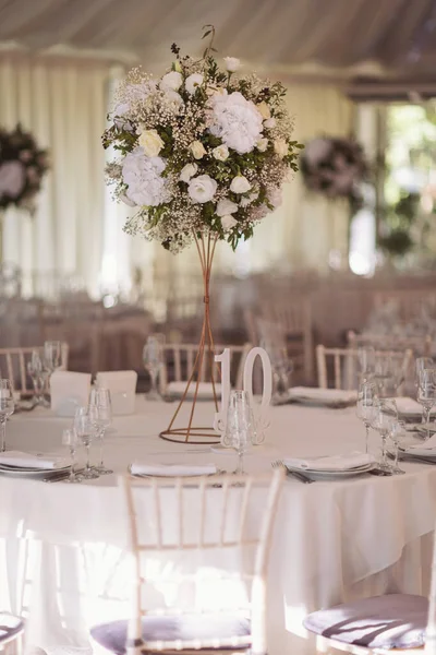 Beautiful flowers on the table on the wedding day. White color wedding table decorated with decorative and elegant flowers for wedding. There are flowers and serving plates on the wedding table.
