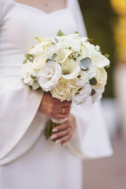 Gelin elinde güzel beyaz bir düğün buketi tutuyor. Şehvetli bir düğün çifti. Yeni evlilerin romantik anları. Düğün fotoğrafı. Gelinin özel gününde tuttuğu düğün çiçekleri..