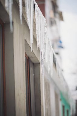 Buz saçakları bir evin çatısında asılı. Evin çatısından sarkan buz saçakları olan kış manzarası. Buz saçakları, kar şapkası. Buz sarkıtı üzerine yumuşak bir odak noktası. Hava durumu. Meteoroloji. 