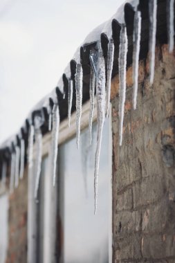 Buz saçakları bir evin çatısında asılı. Evin çatısından sarkan buz saçakları olan kış manzarası. Buz saçakları, kar şapkası. Buz sarkıtı üzerine yumuşak bir odak noktası. Hava durumu. Meteoroloji. 