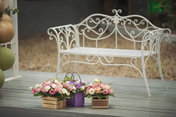 bouquets of beautiful flowers in a wooden pot on the terrace. Vintage box with colorful flowers and white elegant chair on the background. Decorative element from wooden boxes and fresh flowers.