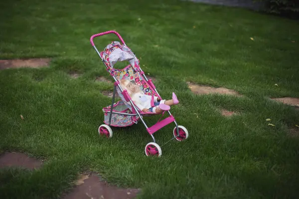 baby stroller with a doll near the lawn. toy stroller on the grass. baby carriage with doll, take care of childred outdoor concept.