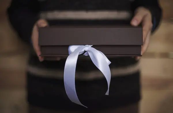 a woman opens a brown box with ribbon. Woman hands holding and opening brown box. Present, packaging, shopping, delivery concept. shipping and home delivery. Surprise.