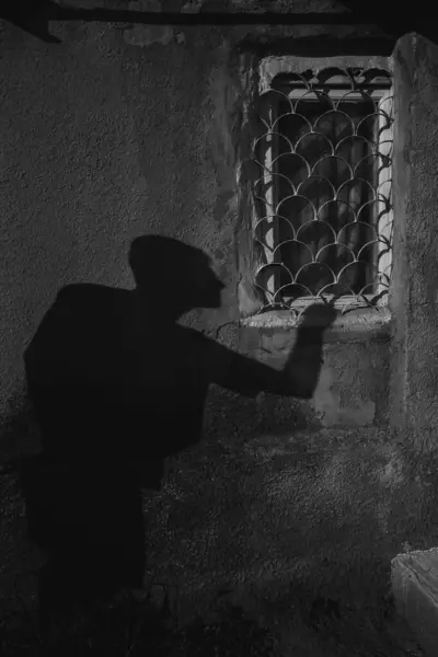 Black and white photo of a Person\'s shadow is on the wall near window, a burglar who climb into the house through the window.