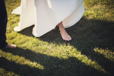 Beyaz elbiseli, yeşil çimenlikte yalınayak güzel ince bacaklı gelin. Yalınayak peçeli gelin yeşil çimlerin üzerinde duruyor 