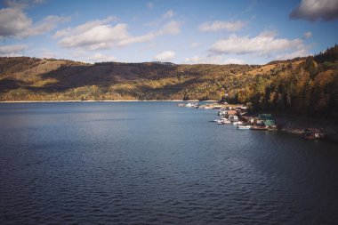 Romanya 'nın Lacul Bicaz kıyısındaki köy manzarası. Dağlardaki ormandaki güzel göl. Sonbaharda akşam ışığında sihirli bir kasabanın havadan çekilmiş görüntüsü.. 