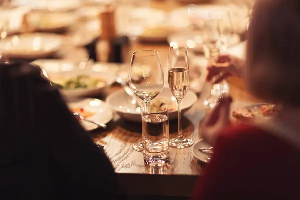 People Dining Together. Luxury served evening banquet at modern restaraunt. Group of diverse friends having a dinner. Restaurant table set with wine glasses and snacks.