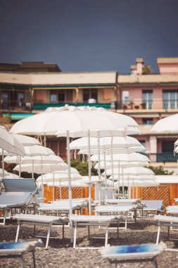 Yağmurdan önceki boş kumsal. Akdeniz kıyıları, boş güneş yatakları, güneşten şemsiyeler, dağlar, çakıl taşları. Otel şezlonglarında plaj şemsiyeleri. Gök gürültülü bir fırtınadan önce deniz kıyısı, seyahat.